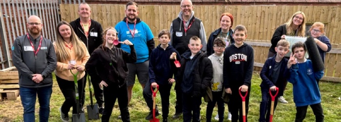 Pupils and volunteers stand proudly in the location of the tree planting with shovels